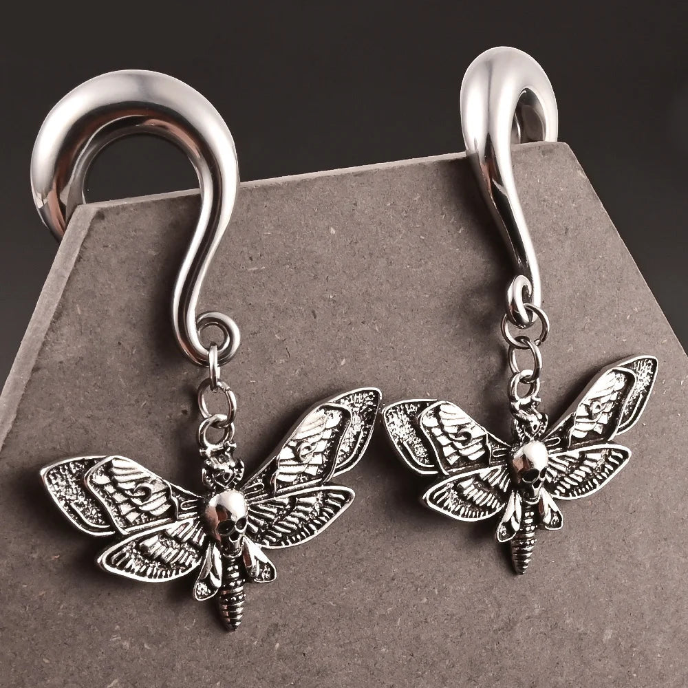 Silver moth-shaped earrings with skull design on a gray background